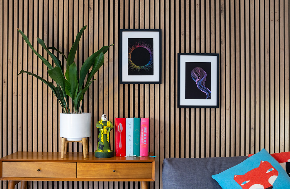 Two colourful pieces of wall art hang side-by-side on a slat wall above a console table with books